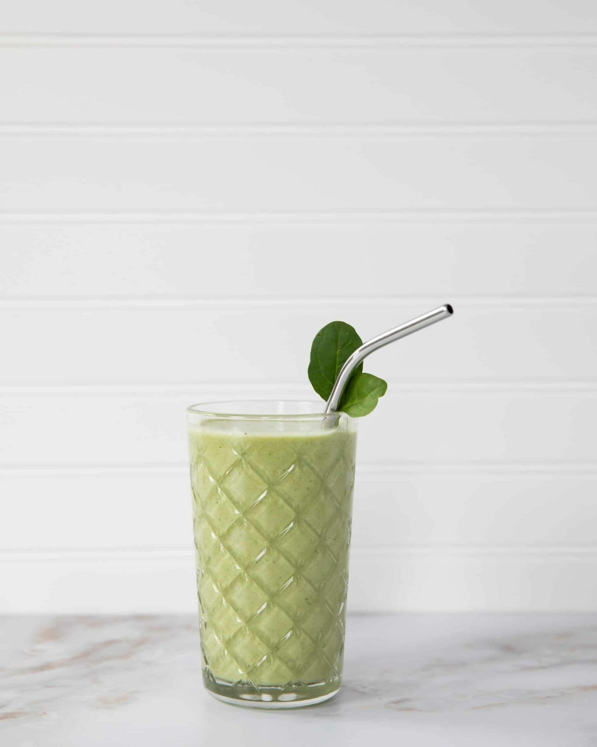 A green drink in a glass, with a metal straw and leaf garnish