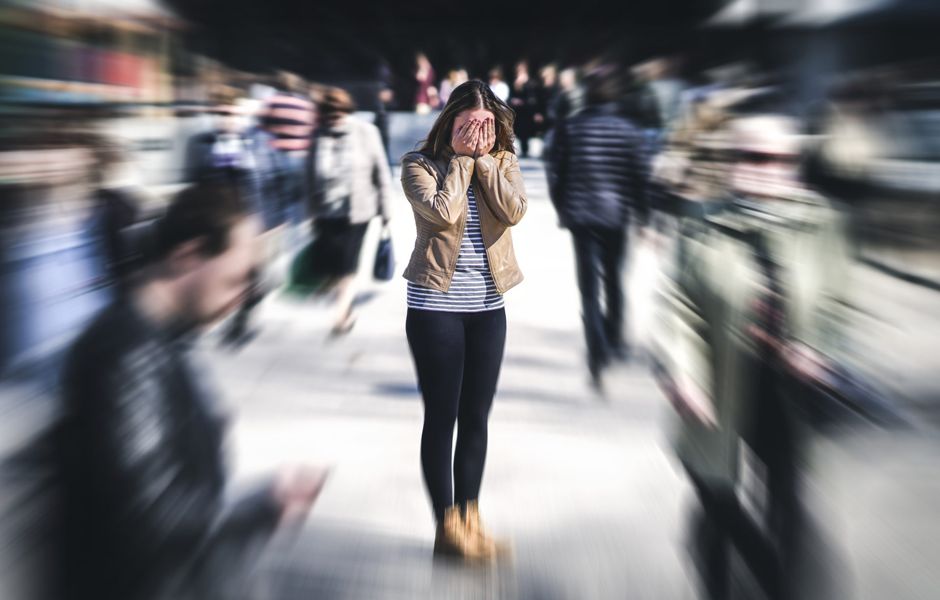A stressed woman covering her face with her hands in a blurred crowded street.