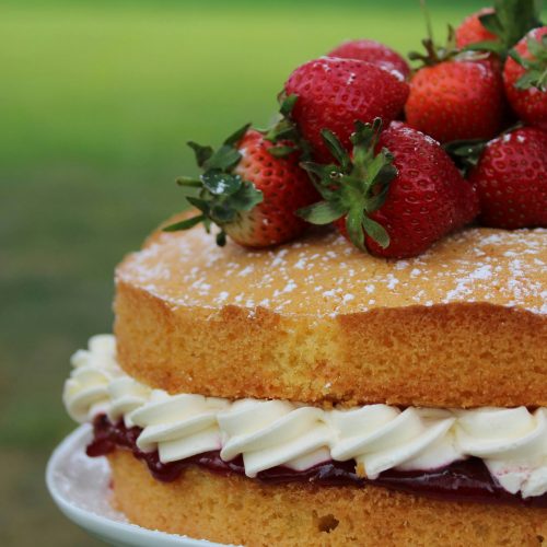 A close up of a victoria sponge cake with strawberries piled on top and a layer of jam and cream through the centre.