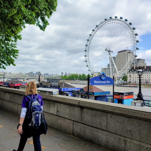 A walker in a purple Deafblind UK t-shirt looks across the Thames to the London Eye.