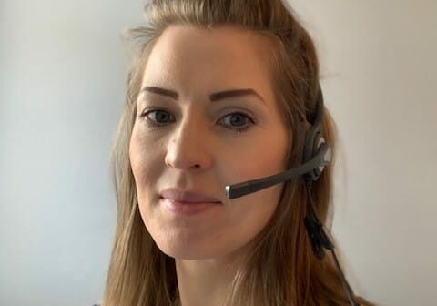 A woman with blond hair wearing a telephone headset and looking at the camera