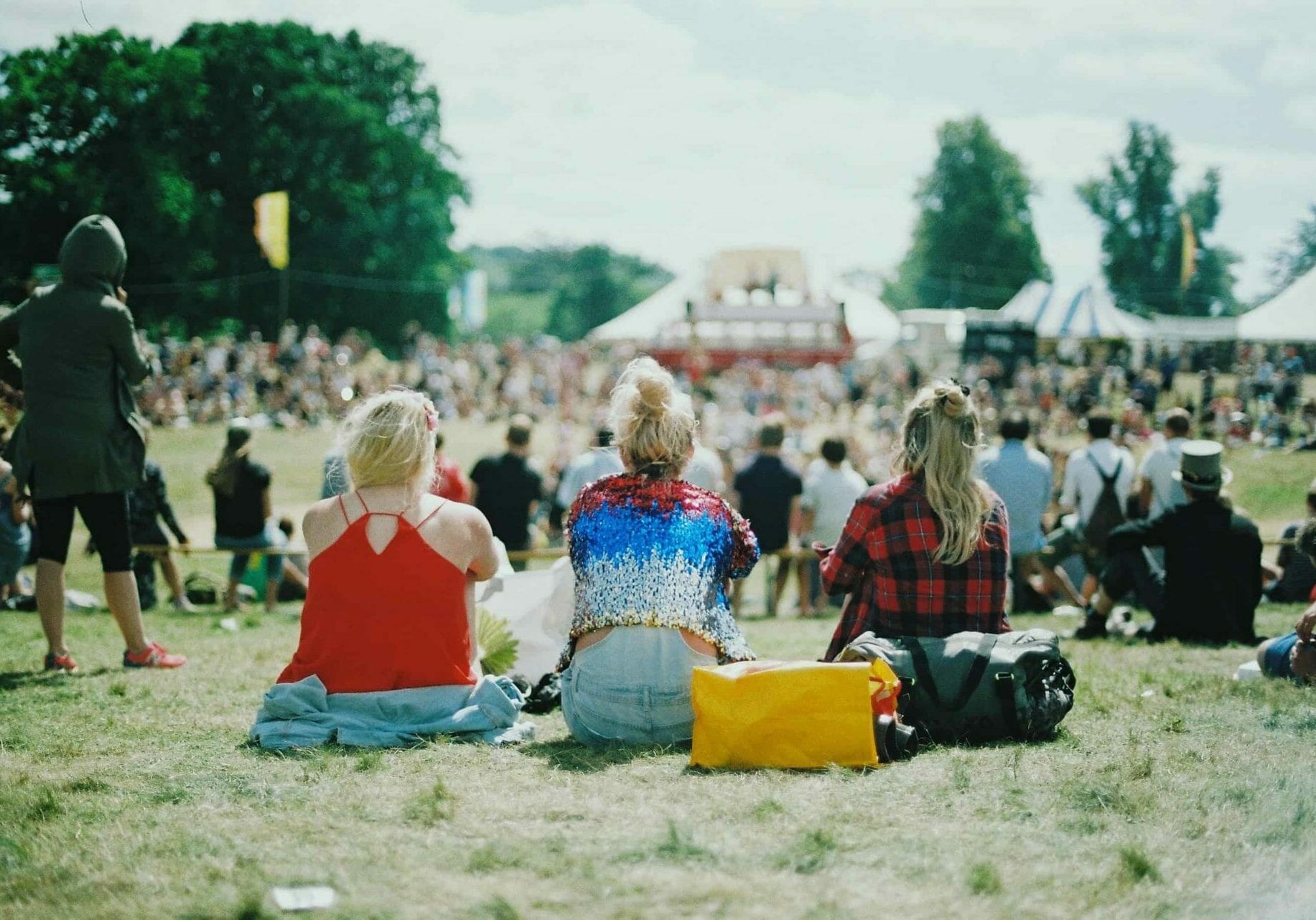 Three people sitting down at a music festival with their backs to the camera